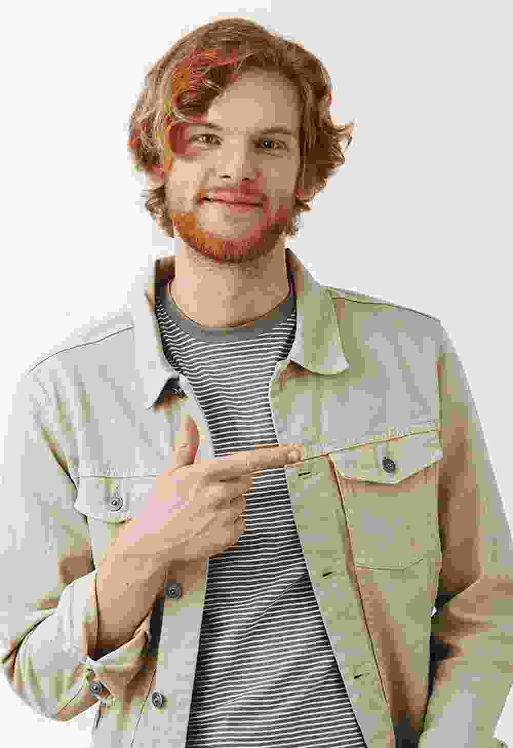 Young man with red hair pointing to his side, smiling.