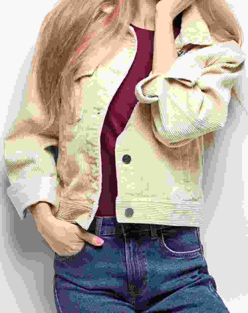 Woman wearing a beige corduroy jacket and blue jeans posing with hand in pocket.