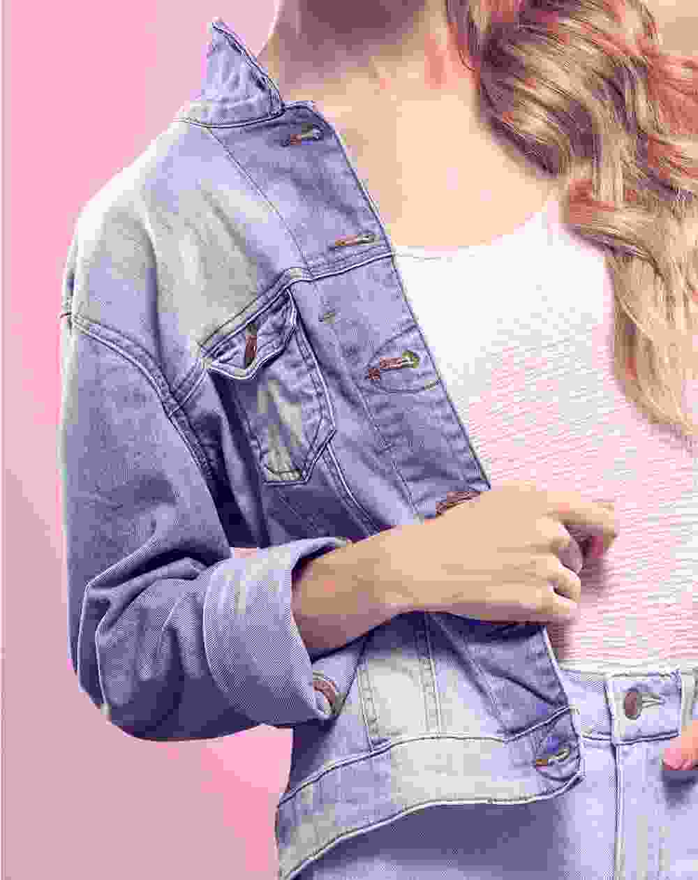 Woman wearing a denim jacket and jeans against a pink background.