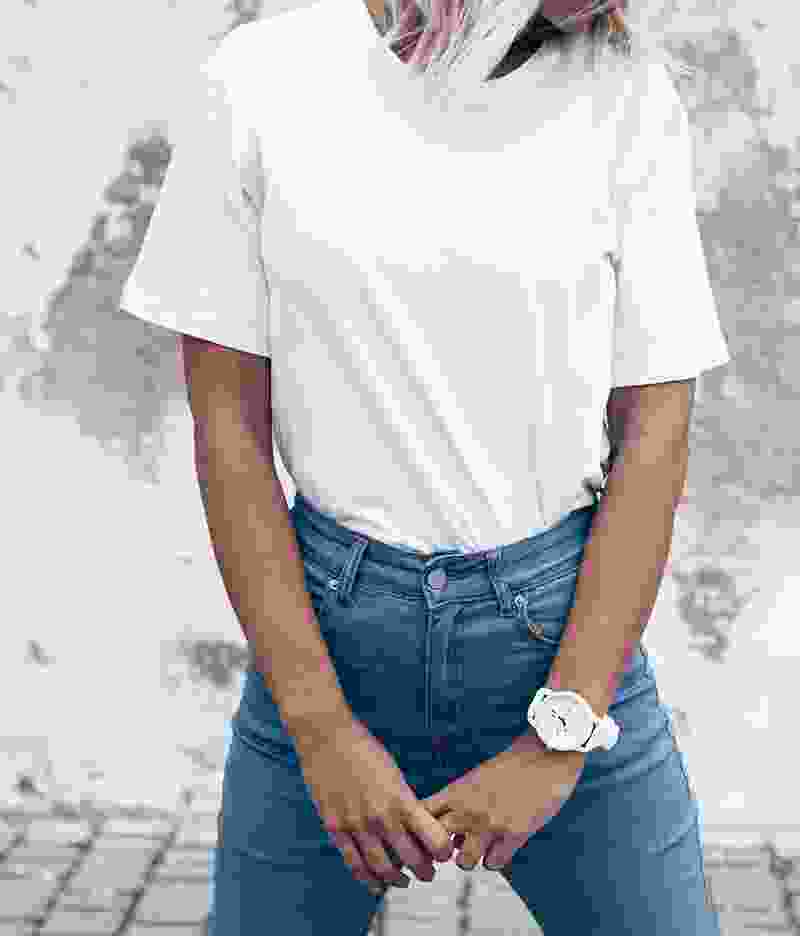 Person wearing a white t-shirt and blue jeans with a white wristwatch.