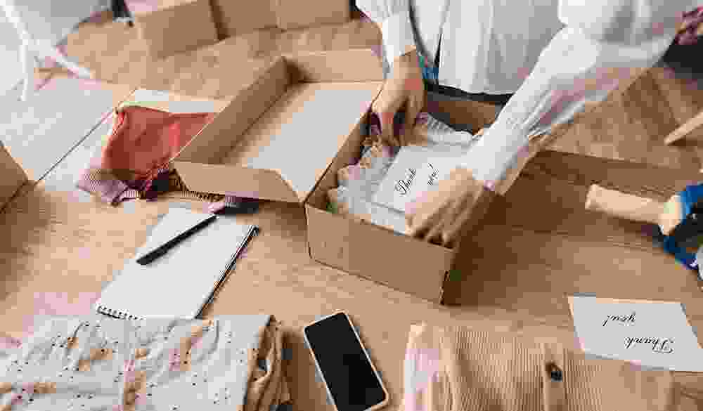 Person packing clothes with thank you card in a cardboard box.