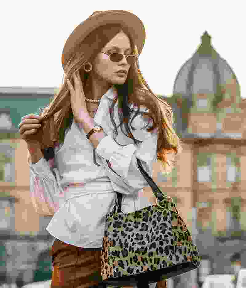 Stylish woman with leopard print bag and sunglasses in urban setting.