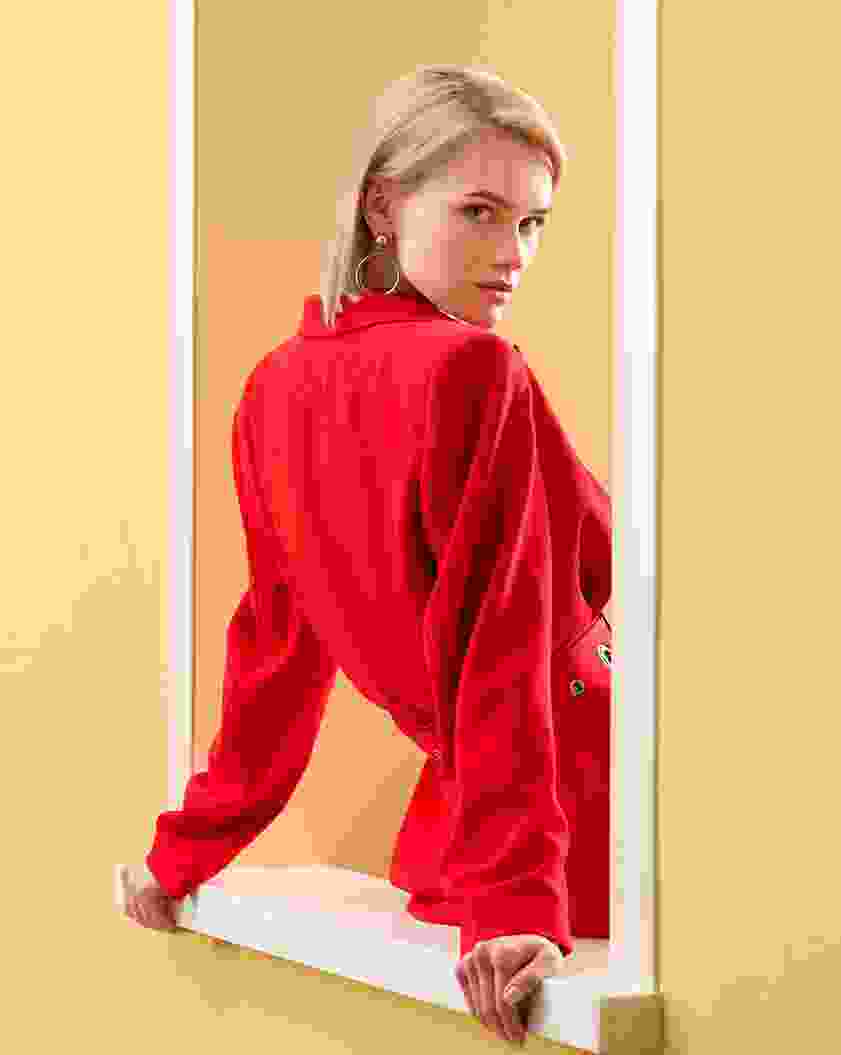 Woman in a vibrant red outfit posing confidently against a beige background.