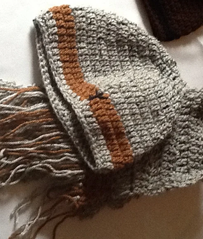 Close-up of a knitted scarf with gray, brown, and orange stripes and fringed ends.