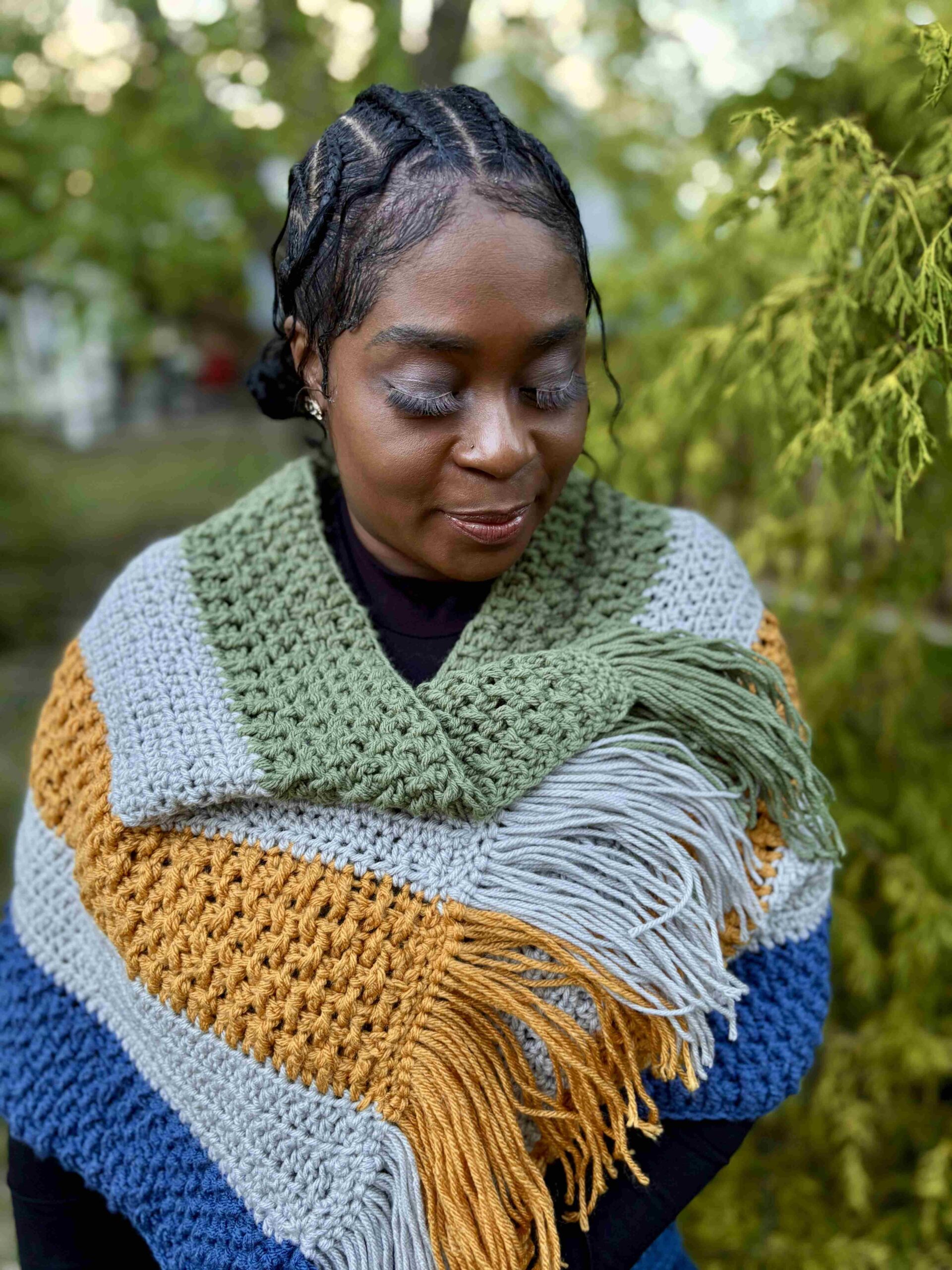 Woman wrapped in a multicolored knitted shawl with fringe details outdoors.